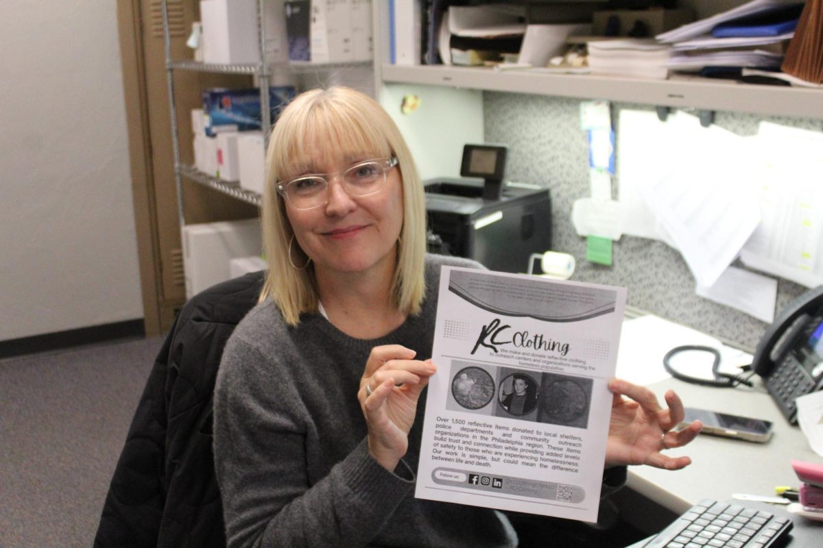 Working for change: Business Office secretary Alice Ciocco poses with a flyer for RC Clothing, promoting the organization and sharing its goals. She started the organization to donate reflective clothing to homeless people in Chester County. 