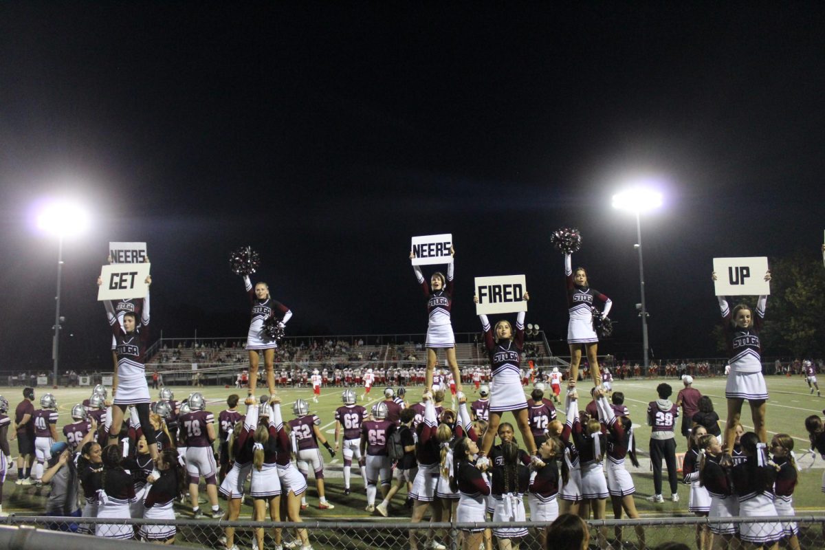 Up high: The cheer team incorporates signs into its sideline stunts during the homecoming game on Sept. 19. The homecoming game was the seventh game they have performed at this season.
